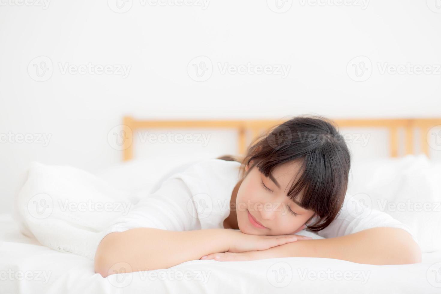 hermosa mujer joven asiática cansada de dormir acostada en la cama cómoda y feliz, chica con relajación y ocio en el concepto de dormitorio, salud y bienestar. foto