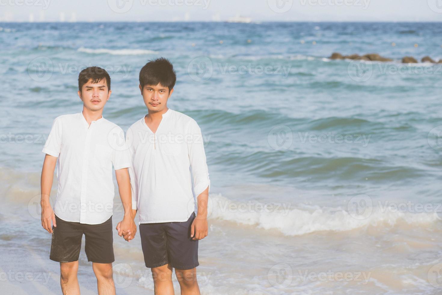 retrato homosexual joven pareja asiática de pie juntos en la playa en verano, asia gay tomados de la mano yendo al mar por placer y relajarse con romántico y feliz en vacaciones en el mar, lgbt con concepto legal. foto