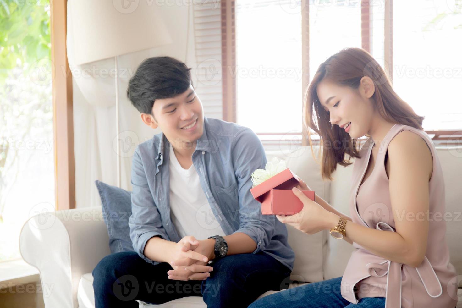 Young asian couple celebrate birthday together, asia man giving gift box present to woman for surprise at living room, female feeling happy and excited anniversary, holiday valentine concept. photo