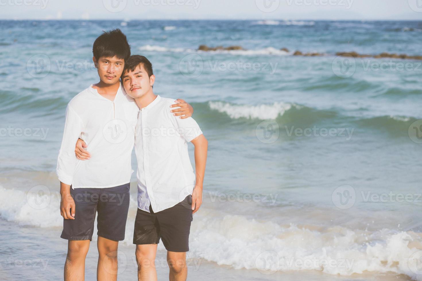 retrato homosexual joven pareja asiática de pie abrazo juntos en la playa en verano, turismo gay de asia para el ocio y relajarse con romanticismo y felicidad en vacaciones en el mar, concepto lgbt. foto