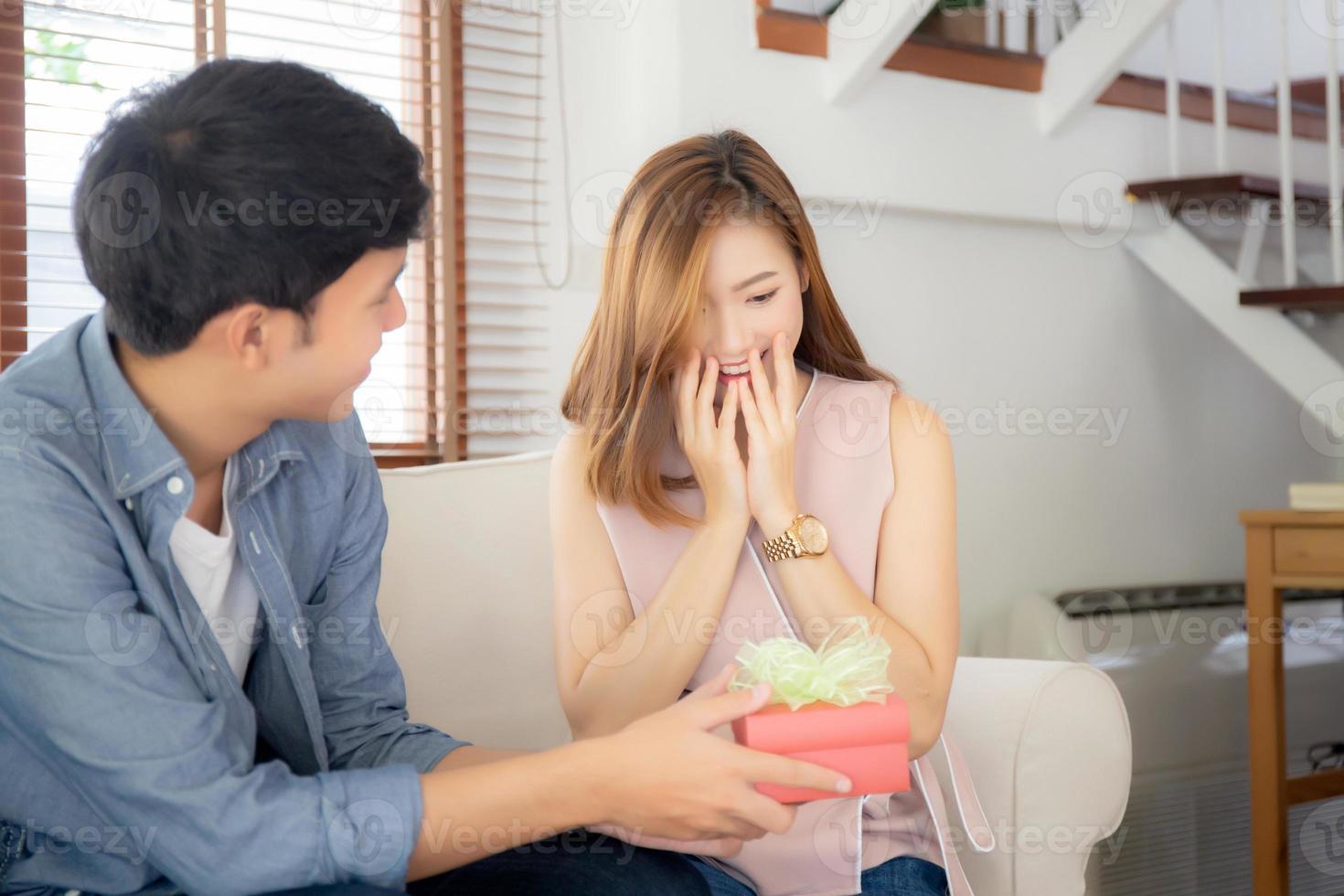 Young asian couple celebrate birthday together, asia man giving gift box present to woman for surprise at living room, female feeling happy and excited anniversary, holiday valentine concept. photo