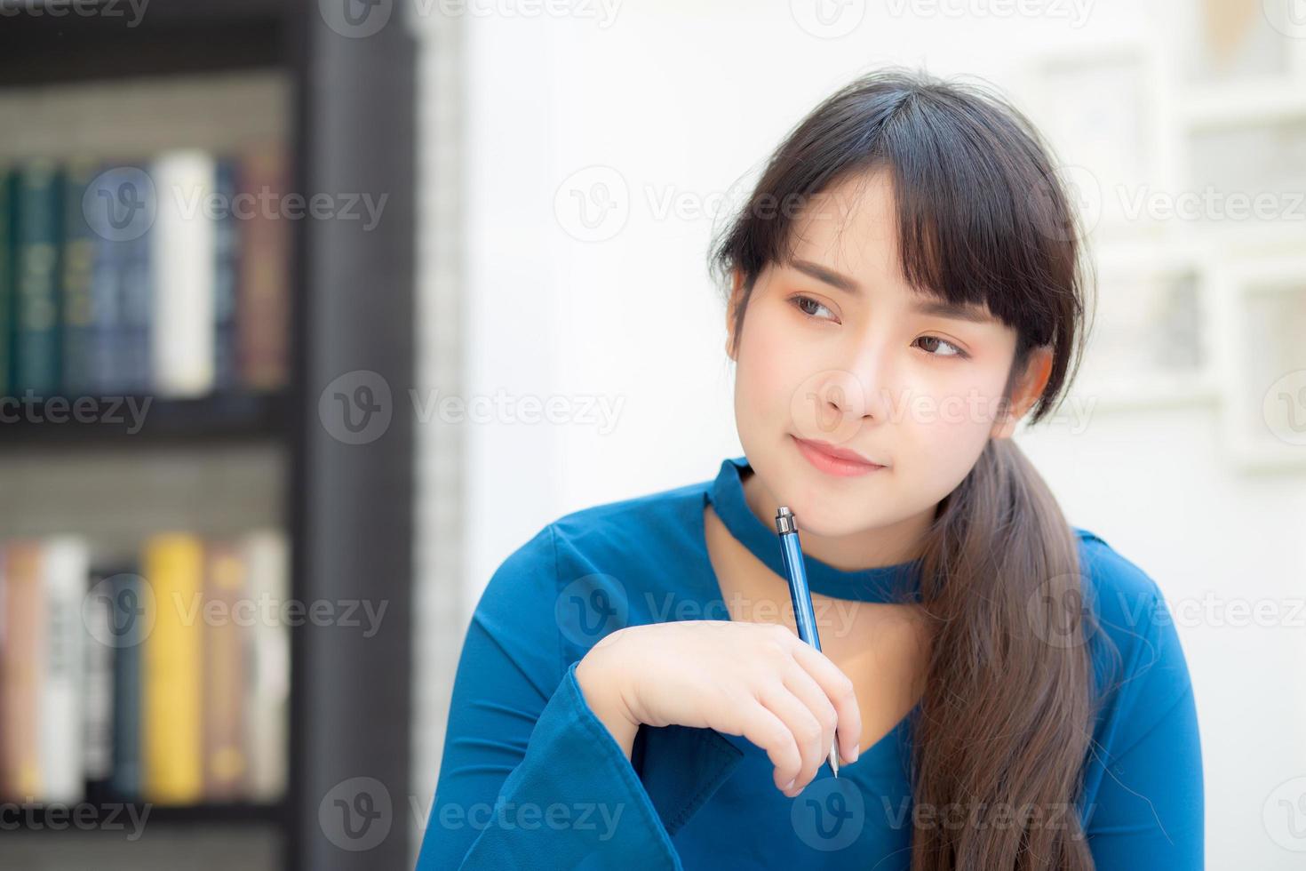 hermosa joven escritora asiática sonriendo pensando en una idea y escribiendo en un cuaderno o diario con feliz estilo de vida de una chica asiática es estudiante, planificación femenina de trabajo, educación y concepto de negocios. foto