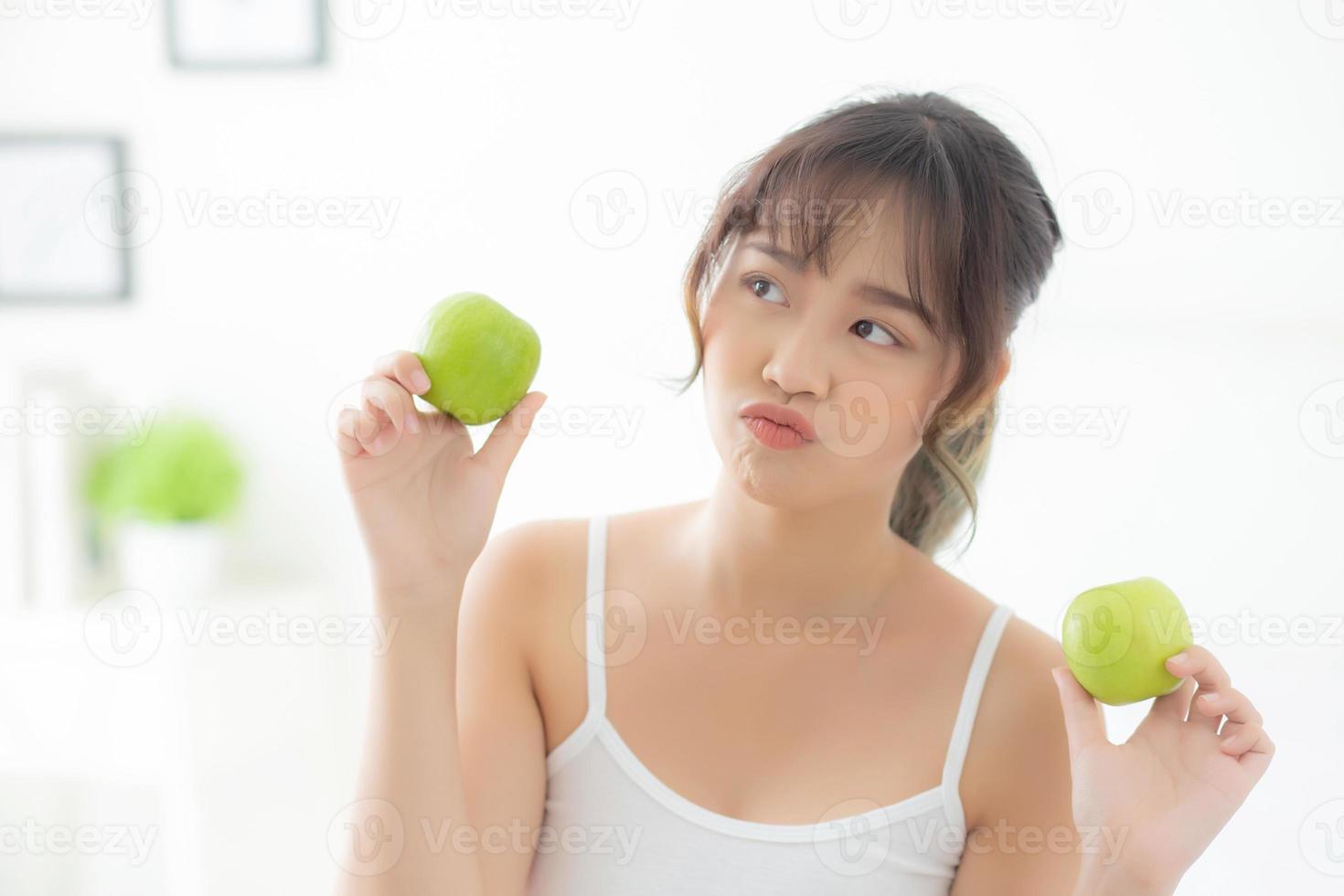 hermoso retrato joven mujer asiática sosteniendo y comiendo fruta de manzana verde en el dormitorio en casa, estilo de vida de nutrición niña saludable y cuidado concepto de pérdida de peso, salud y bienestar. foto