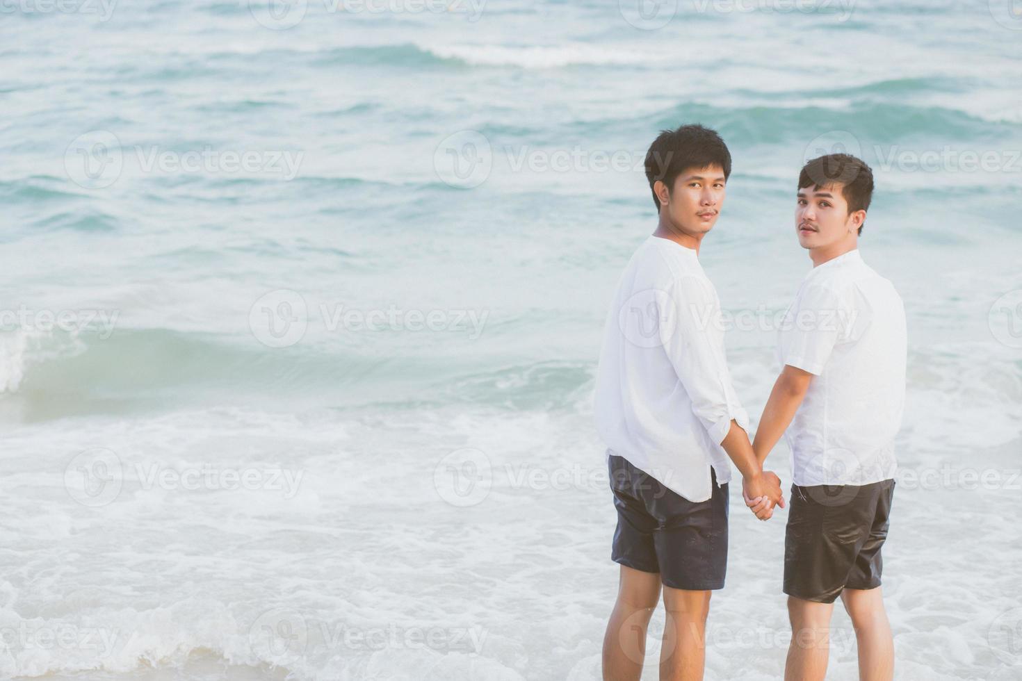 pareja asiática joven homosexual de pie juntos en la playa en verano, asia gay tomados de la mano yendo al mar por placer y relajarse con romántico y feliz en vacaciones en el mar, lgbt con concepto legal. foto