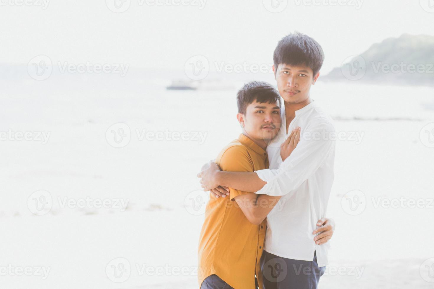 retrato homosexual joven pareja asiática de pie abrazo juntos en la playa en verano, turismo gay de asia para el ocio y relajarse con romanticismo y felicidad en vacaciones en el mar, concepto lgbt. foto