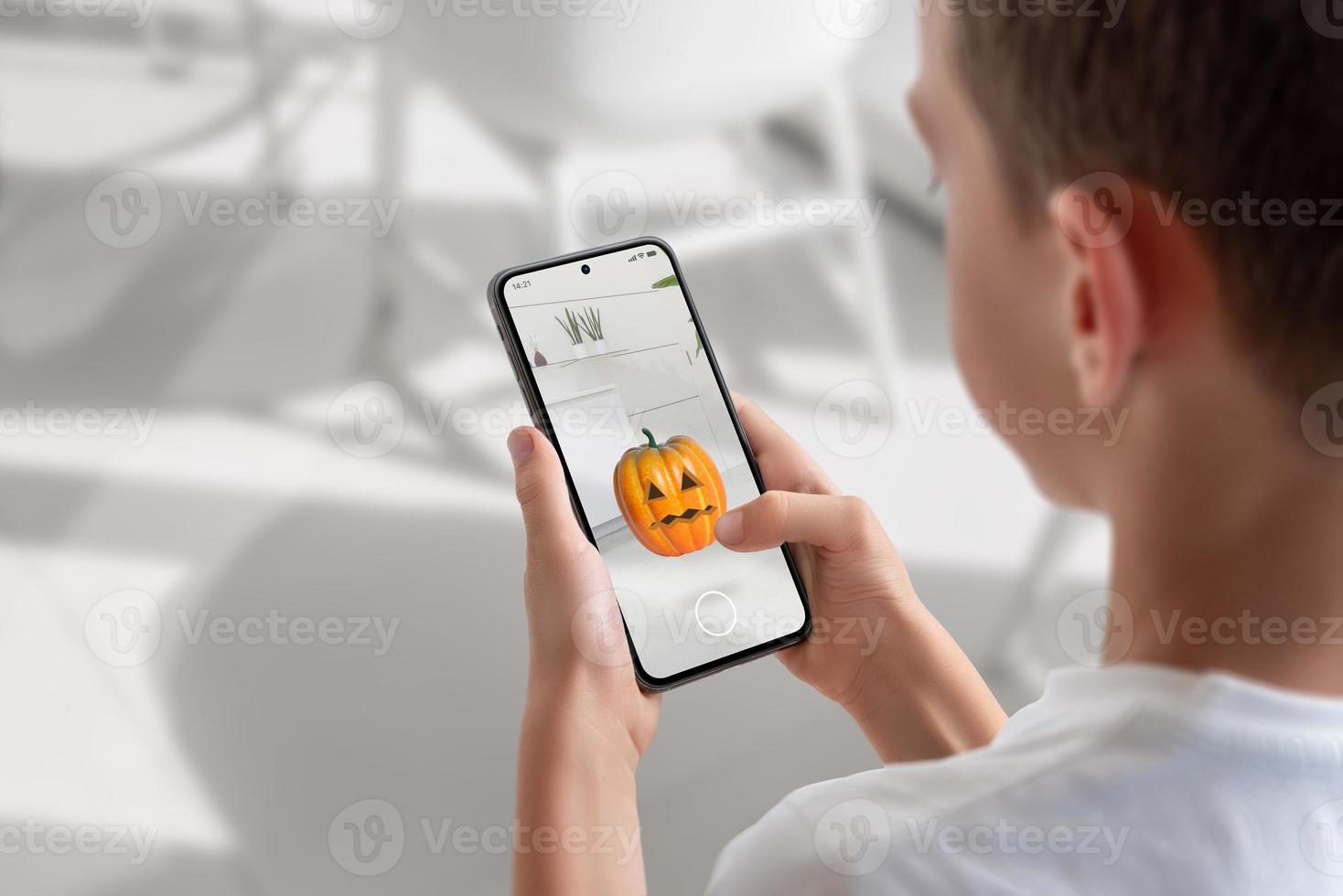 Boy on a mobile phone is playing an augmented reality game. View over shoulder at the phone display. Pumpkin throwing game concept photo