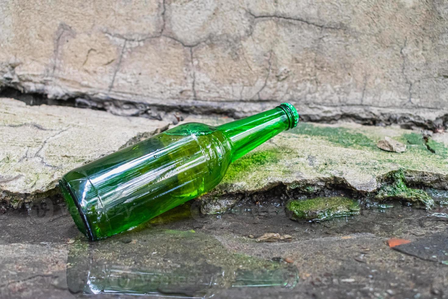 una botella con una bebida alcohólica caducada tirada en un charco en la calle. el problema del alcoholismo en la sociedad foto