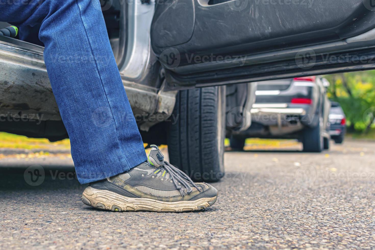 un hombre con jeans y zapatillas sale del auto foto