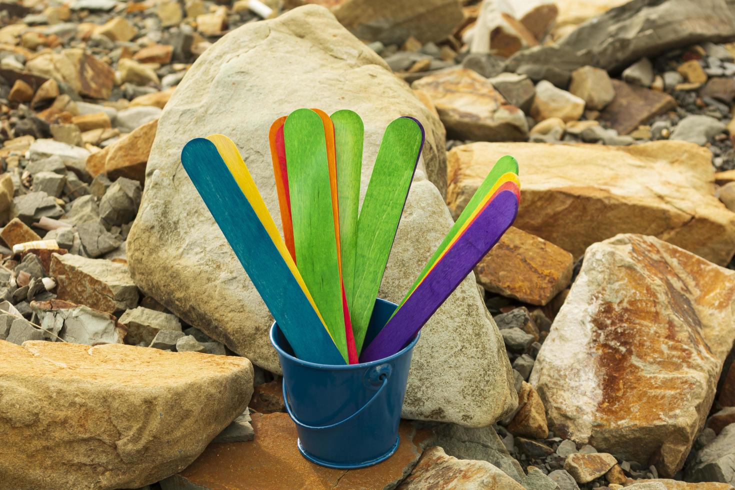 Colorful wooden sticks inside of a blue bucket with stone beach background. photo