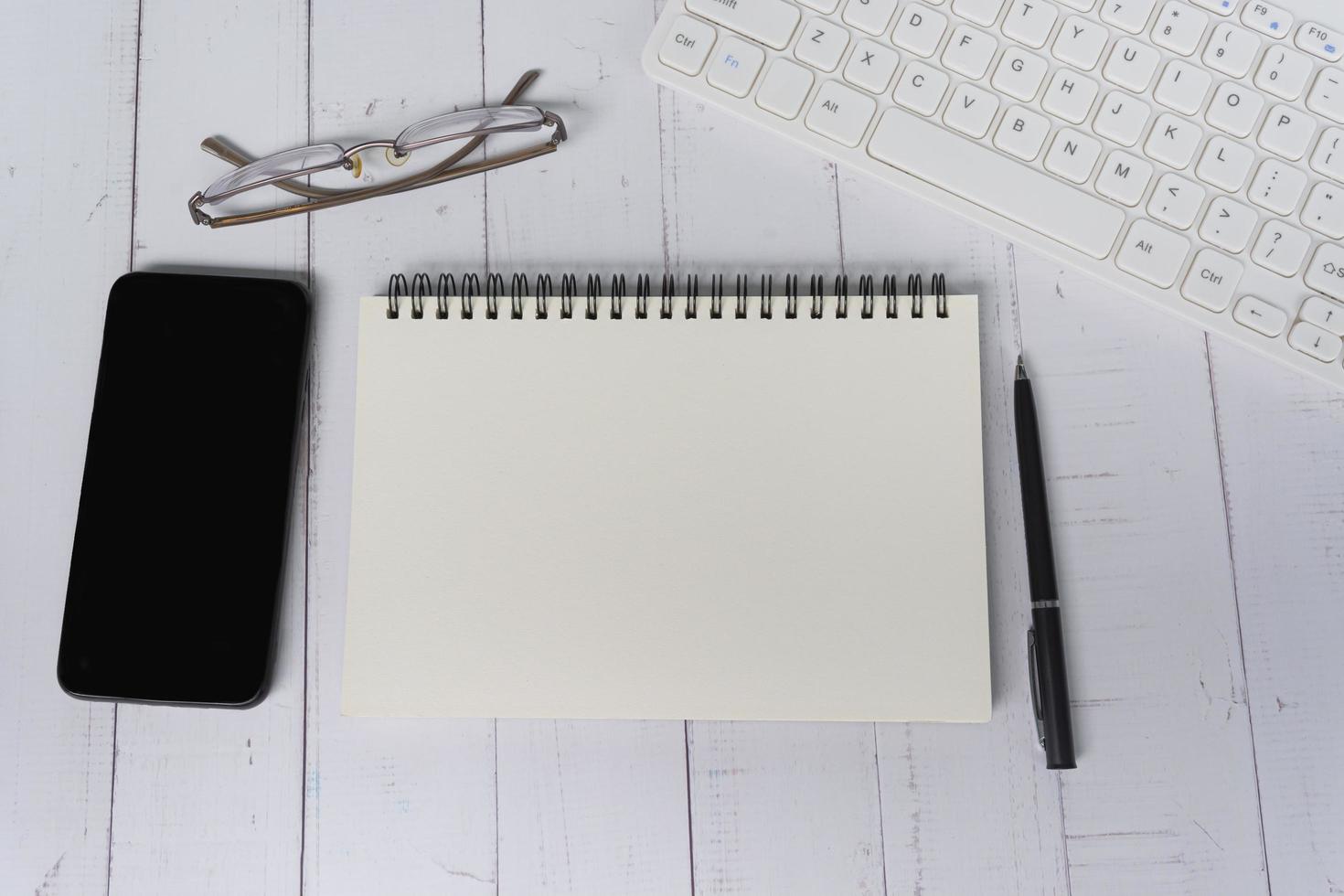 Notepad with computer keyboard, smartphone, pen and reading glasses on a desk. photo