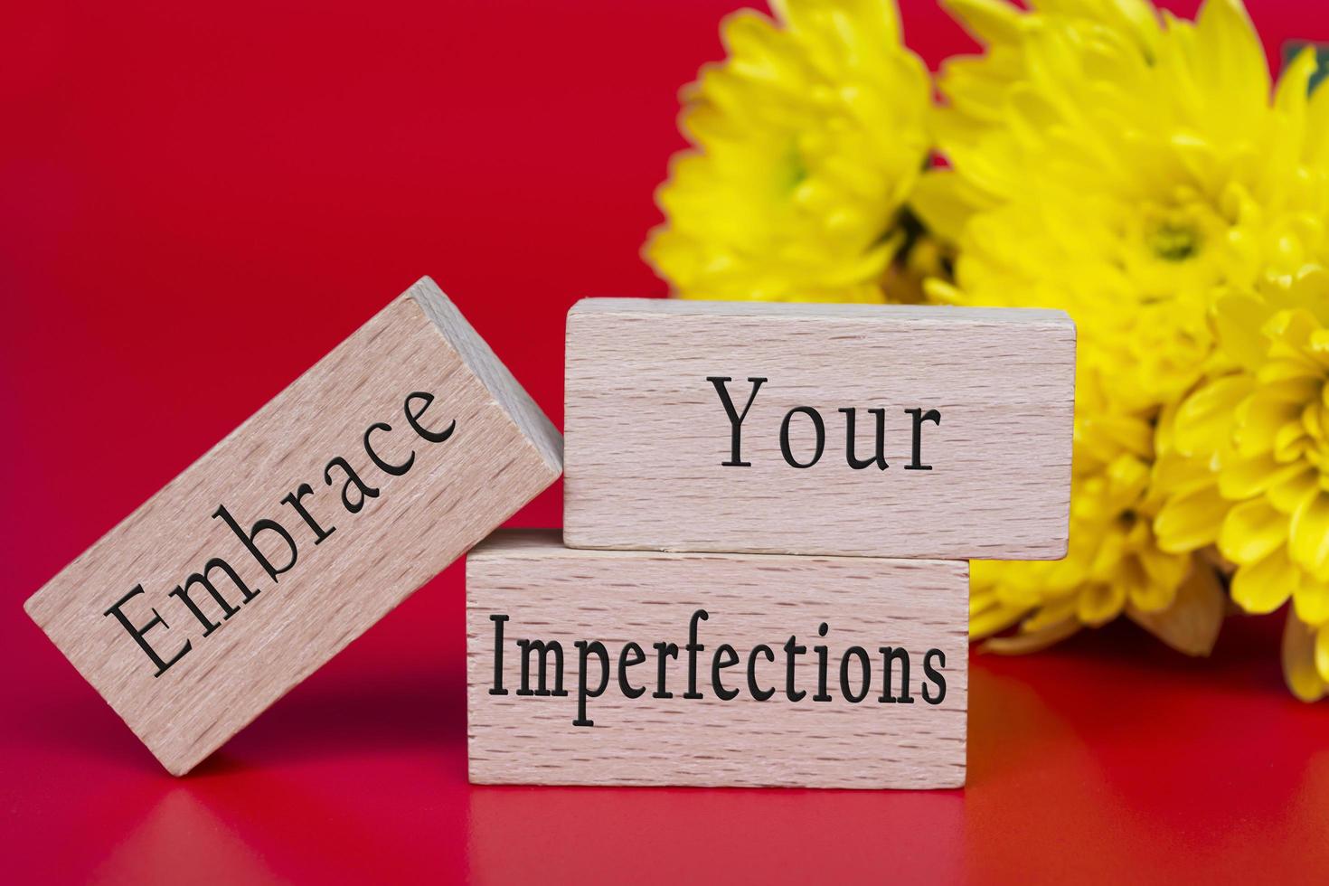 Embrace your imperfections text on wooden cube and with flowers background. photo