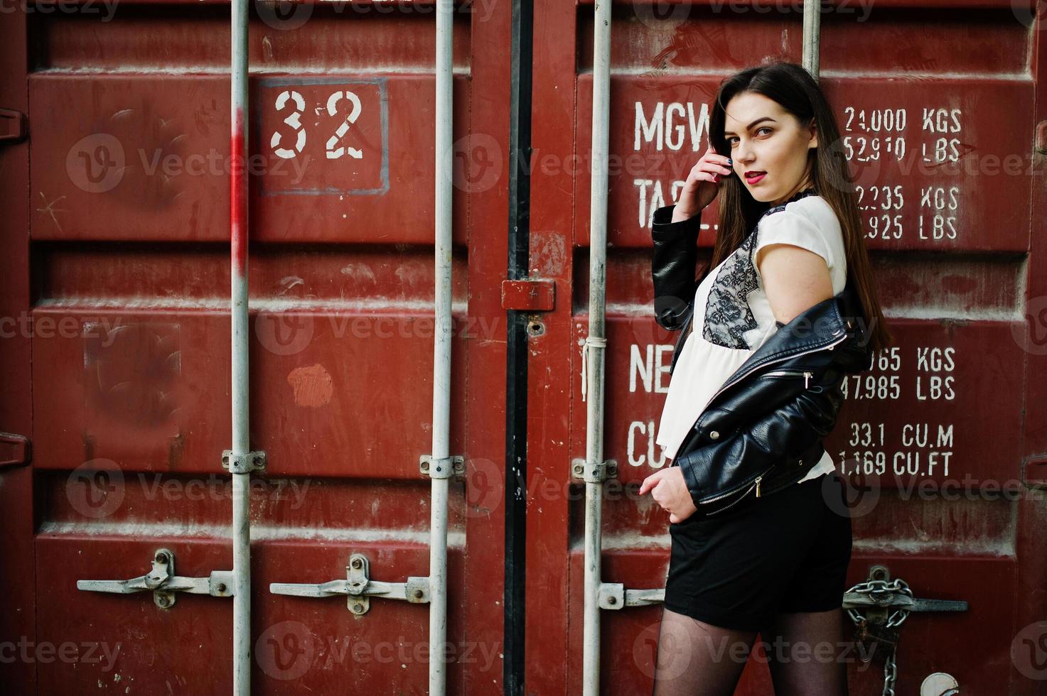 Stylish brunette girl wear on leather jacket and shorts against shipping container. photo