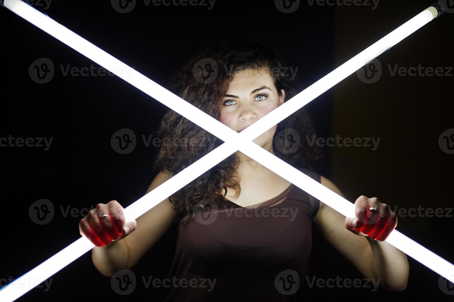 Curly brunette plus size model with two long led lamp at black room. photo