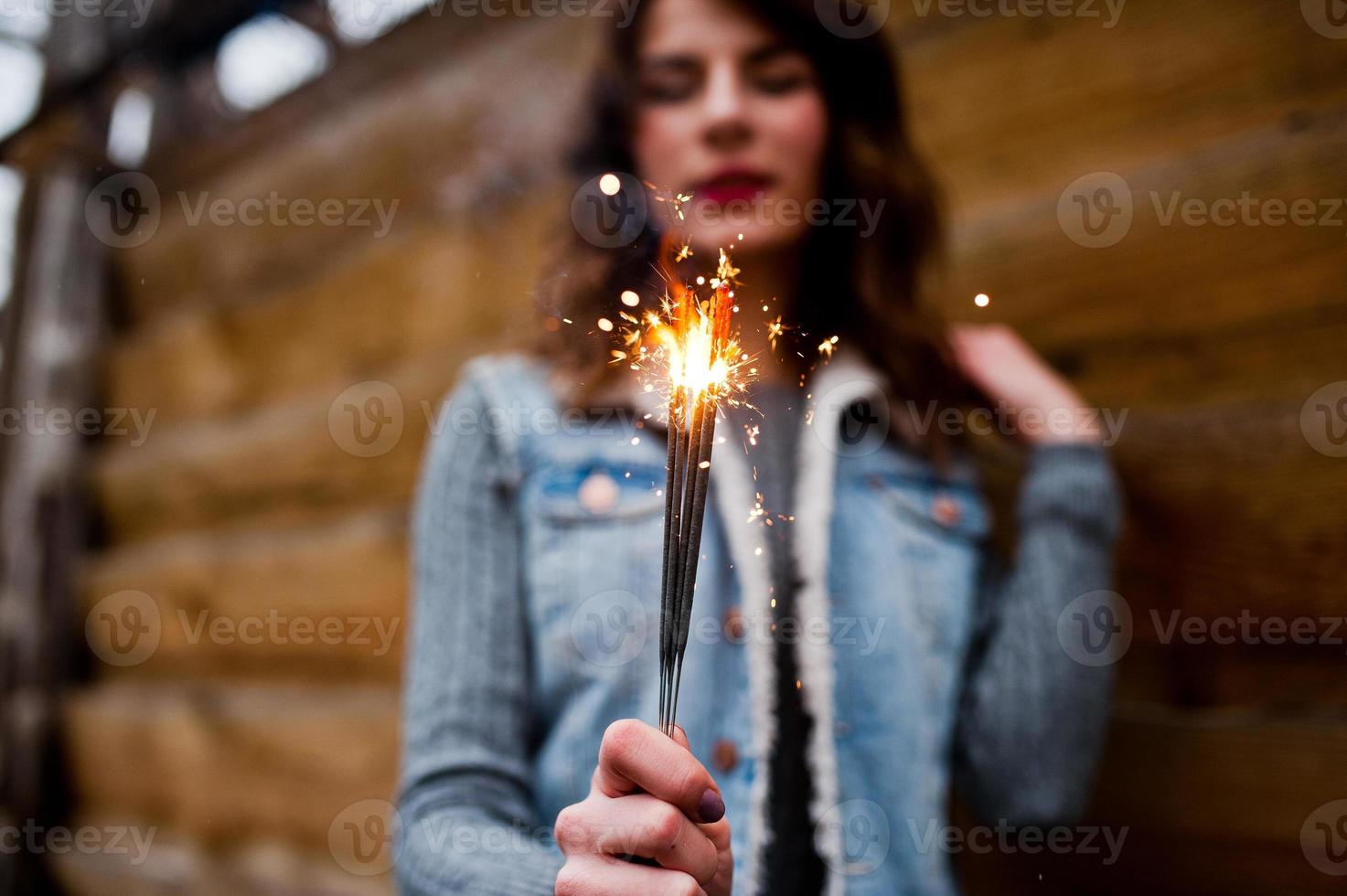 Portrait of brunette girl in jeans jacket with bengal lights in hands. photo