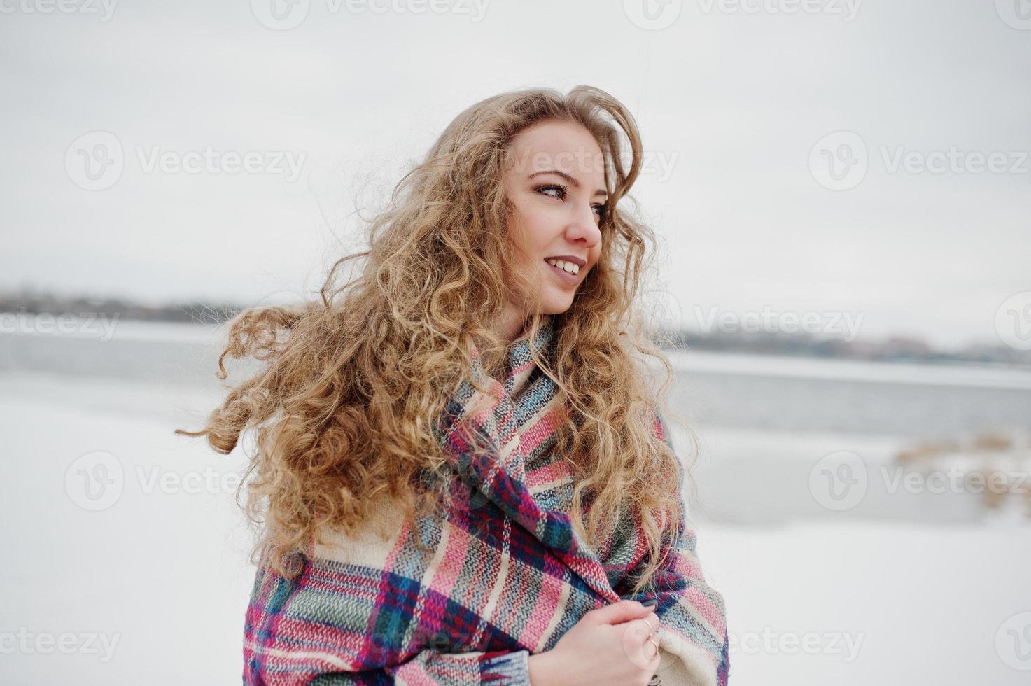 Curly blonde girl in checkered plaid against frozen lake at winter day. photo