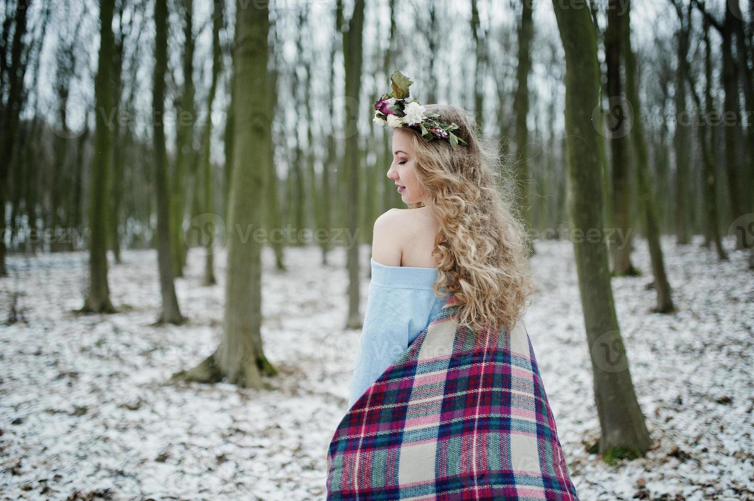 Curly cute blonde girl with wreath in checkered plaid at snowy forest in winter day. photo