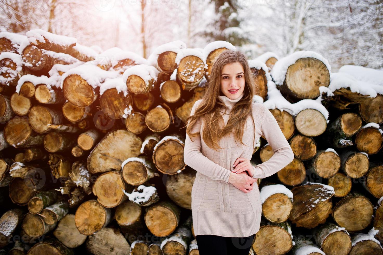 Beautiful brunette girl in winter warm clothing. Model on winter sweater near stump. photo