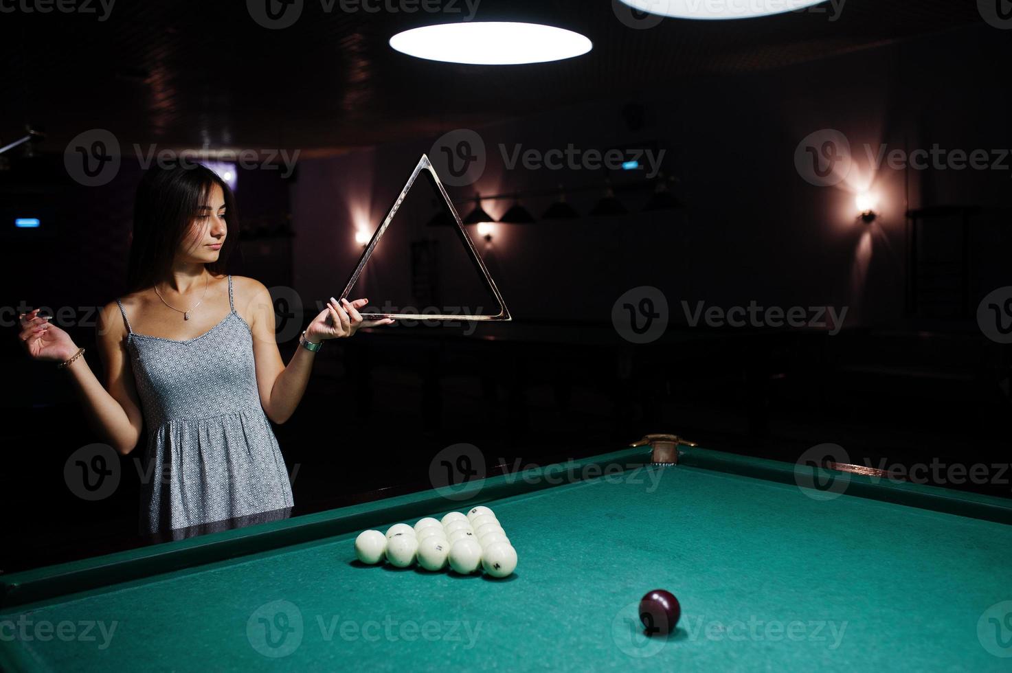 Portrait of a confused woman posing with a triangle by the pool table. photo