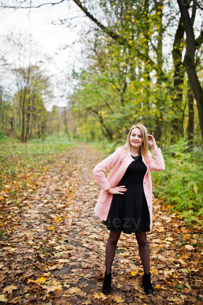 Young blonde girl at pink coat posed on autumn park. photo