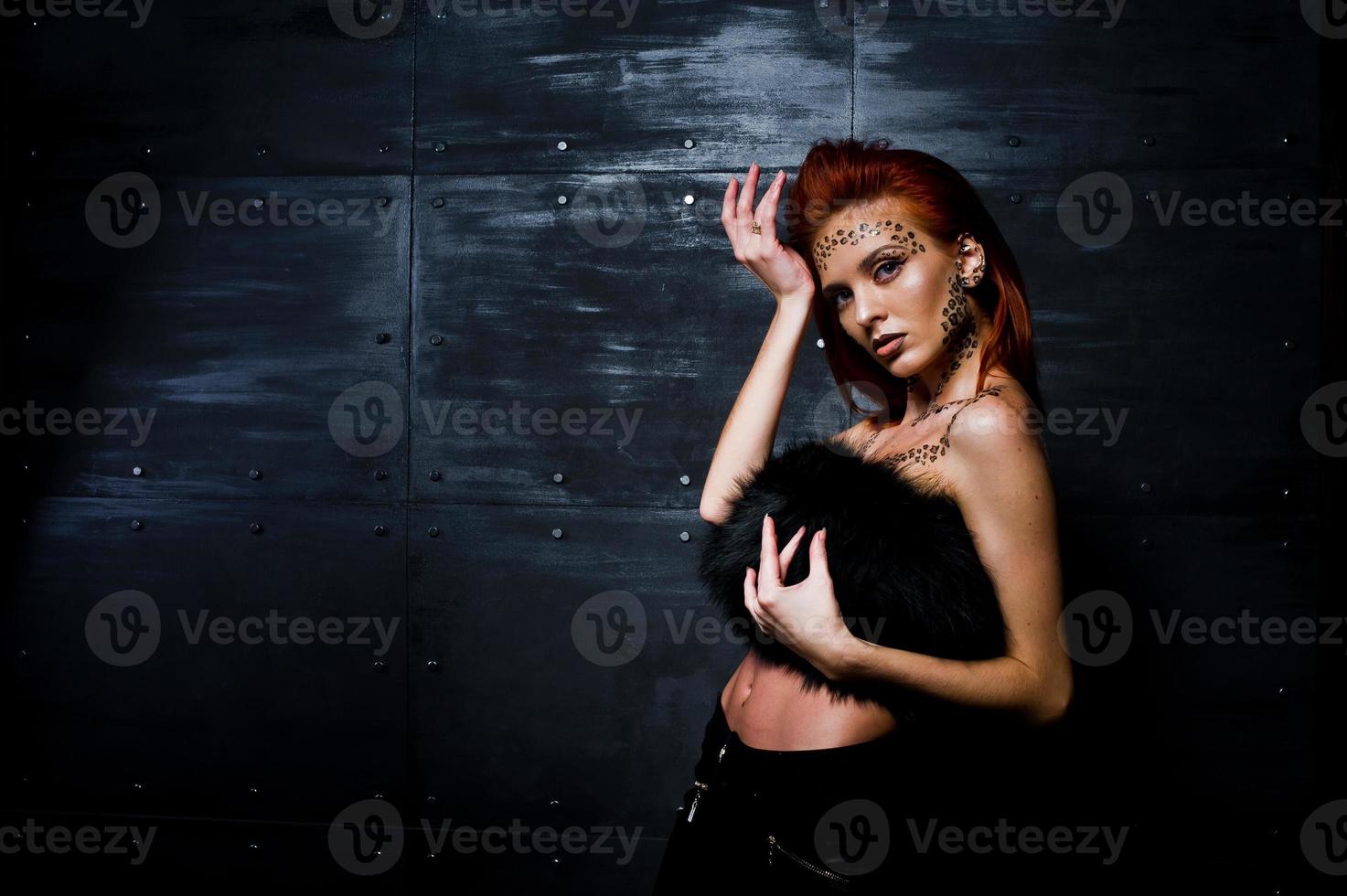 Fashion model red haired girl with originally make up like leopard predator against steel wall. Studio portrait. photo