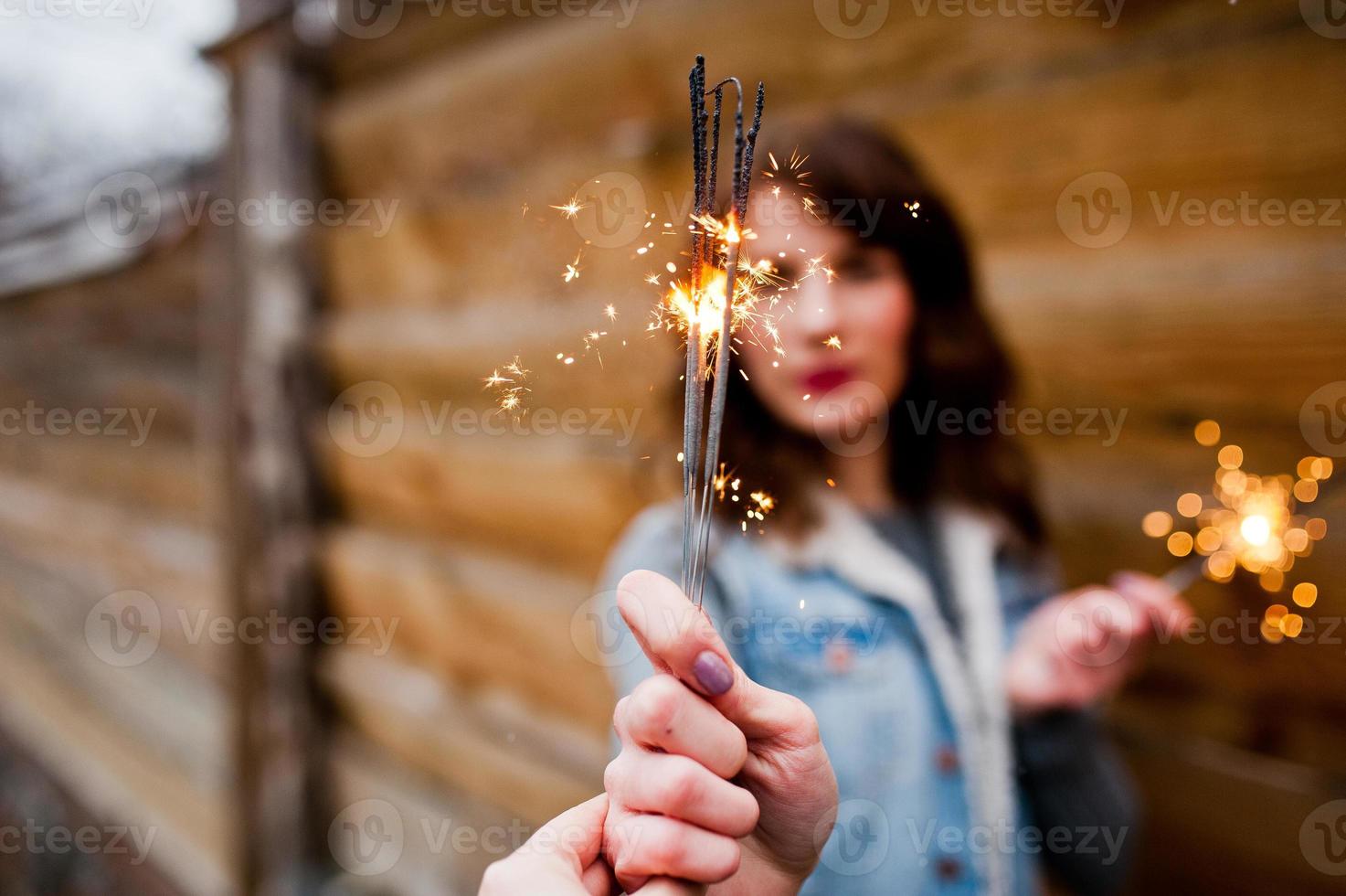 Portrait of brunette girl in jeans jacket with bengal lights in hands. photo