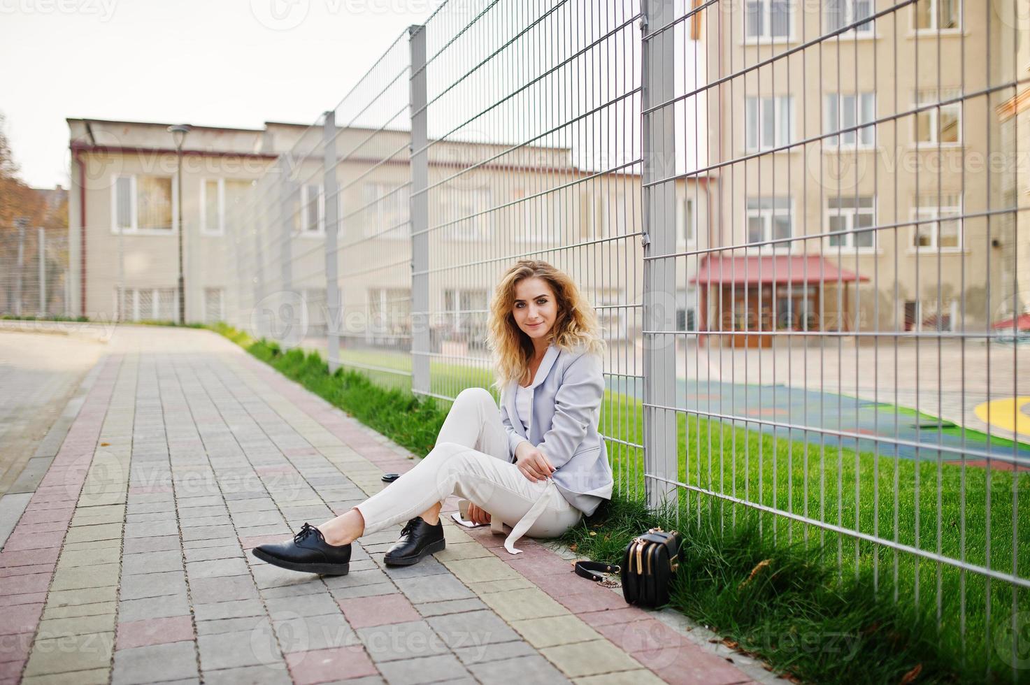 Stylish curly blonde model girl wear on white posing against fence. photo