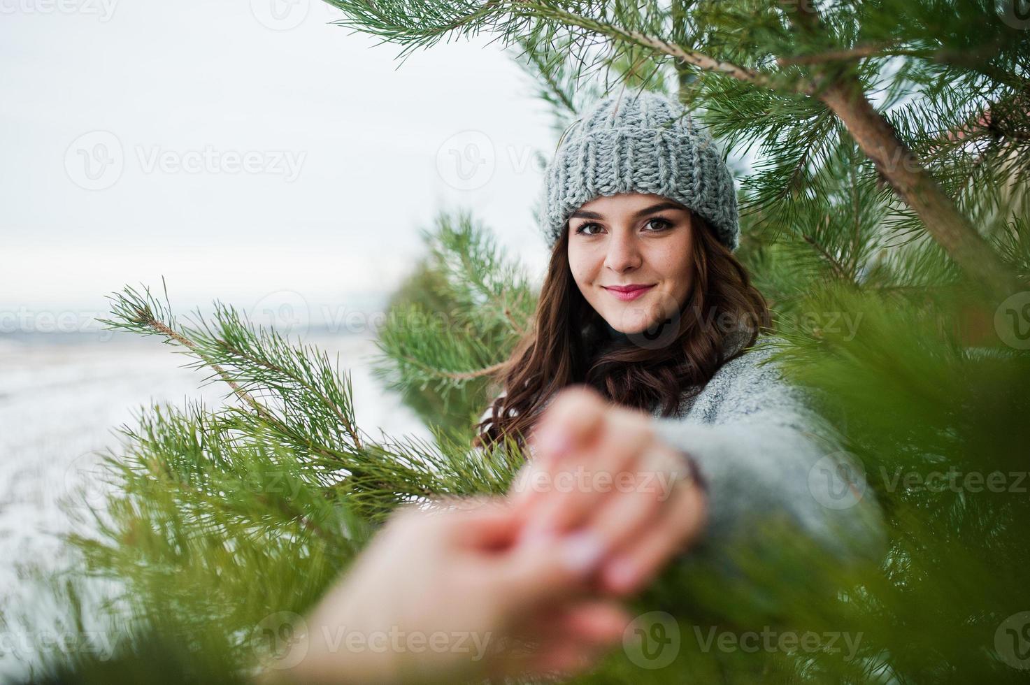 Portrait of gentle girl in gray coat and hat against new year tree outdoor holding hand. photo