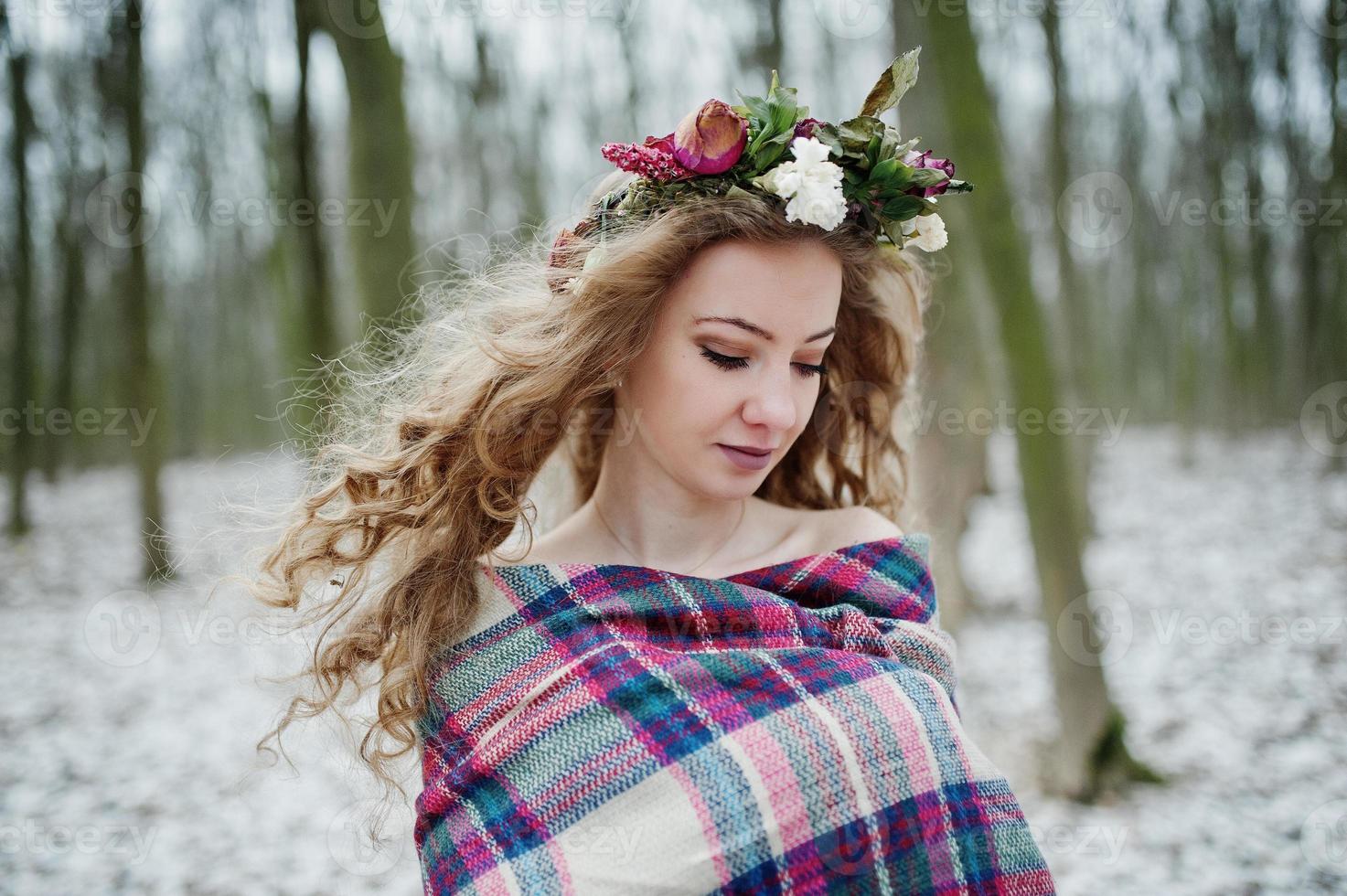 Curly cute blonde girl with wreath in checkered plaid at snowy forest in winter day. photo