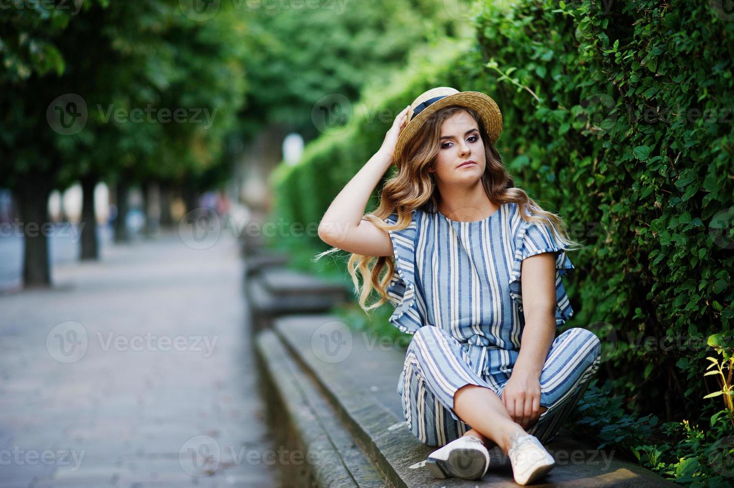 Portrait of a stunning young woman in striped overall sitting in the park. photo