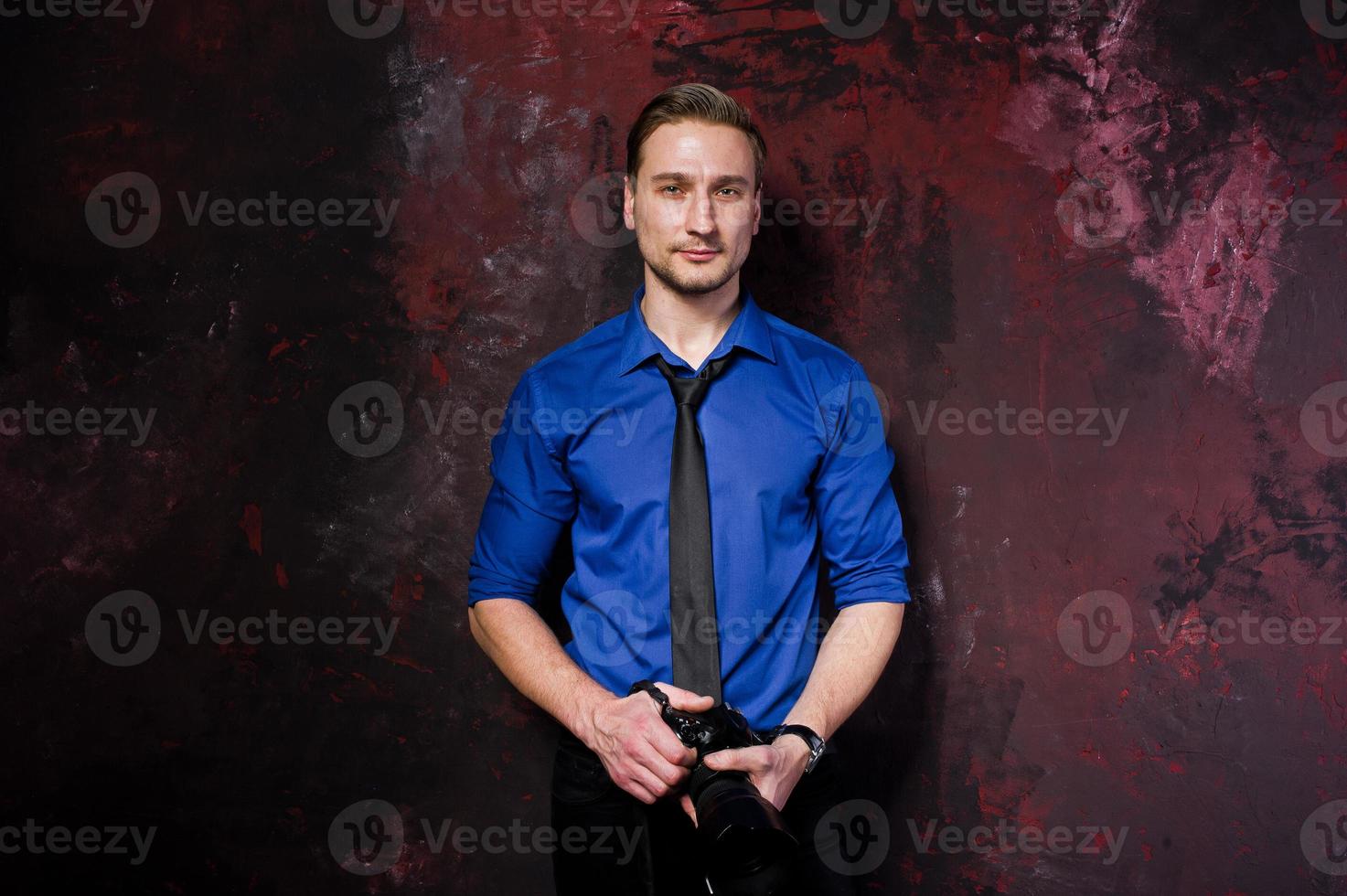 retrato de estudio de un elegante fotógrafo profesional con cámara, vestido con camisa azul y corbata. foto