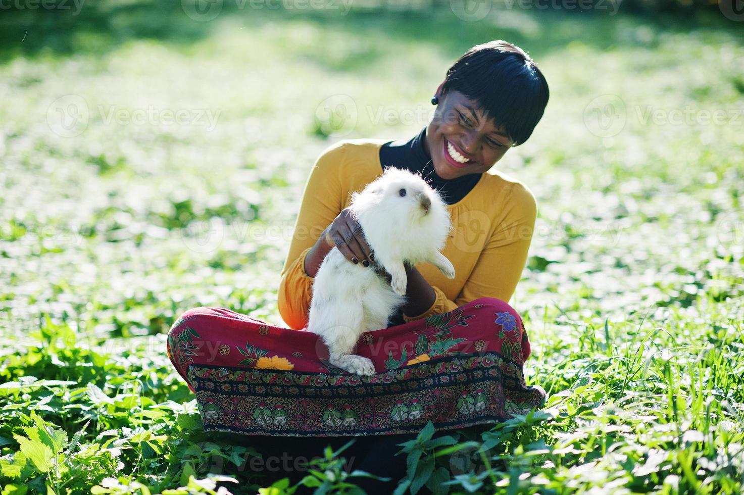 African american girl at yellow and red dress with white rabbit at hands. photo