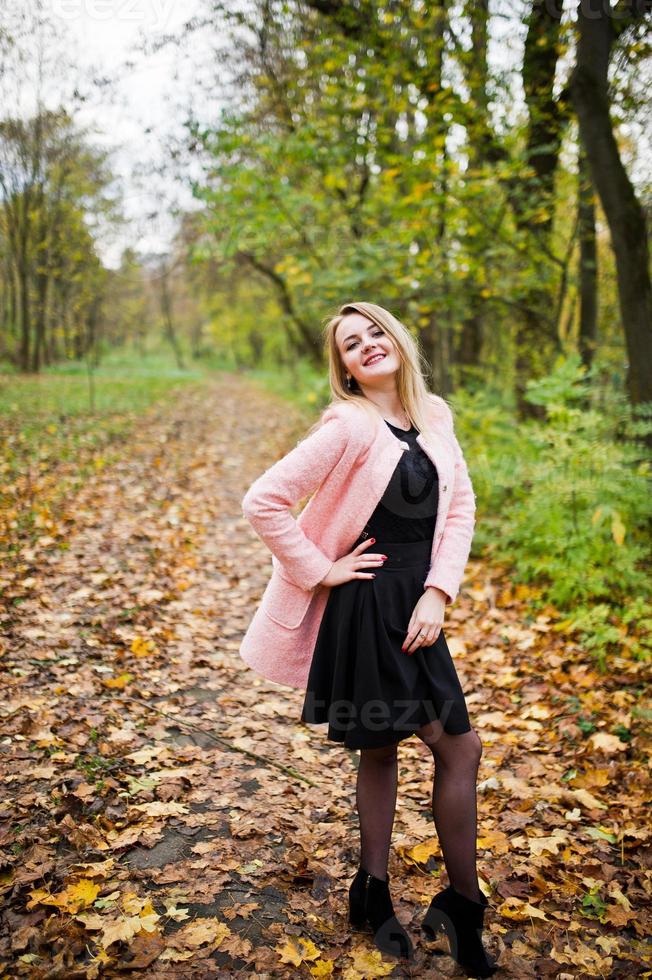 Young blonde girl at pink coat posed on autumn park. photo