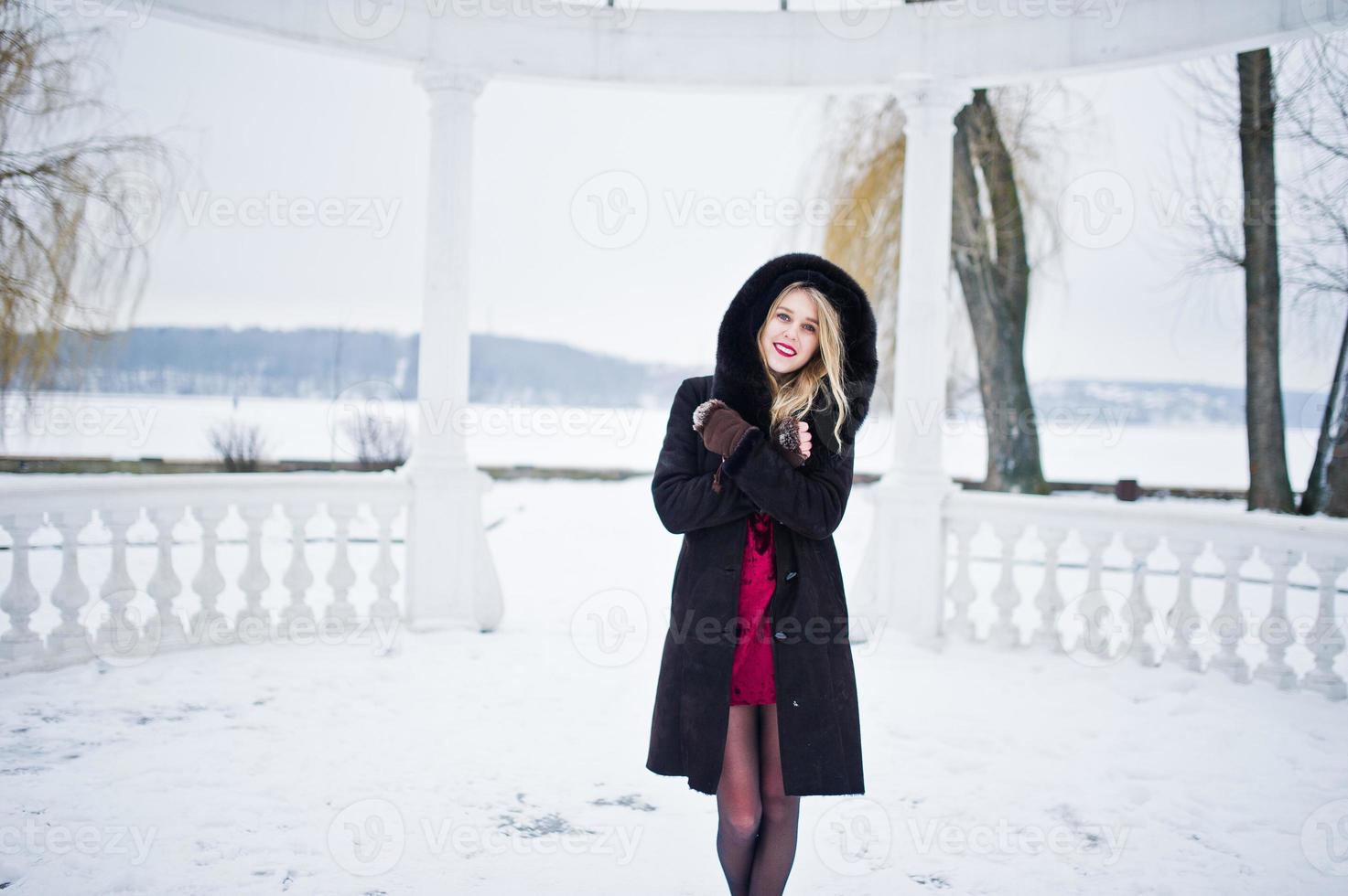 Elegance blonde girl in fur coat and red evening dress posed at winter snowy day. photo
