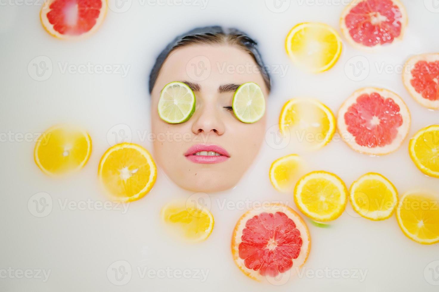 Sexy brunette girl at the bathroom with milk and fruits. Youth bath for body. photo