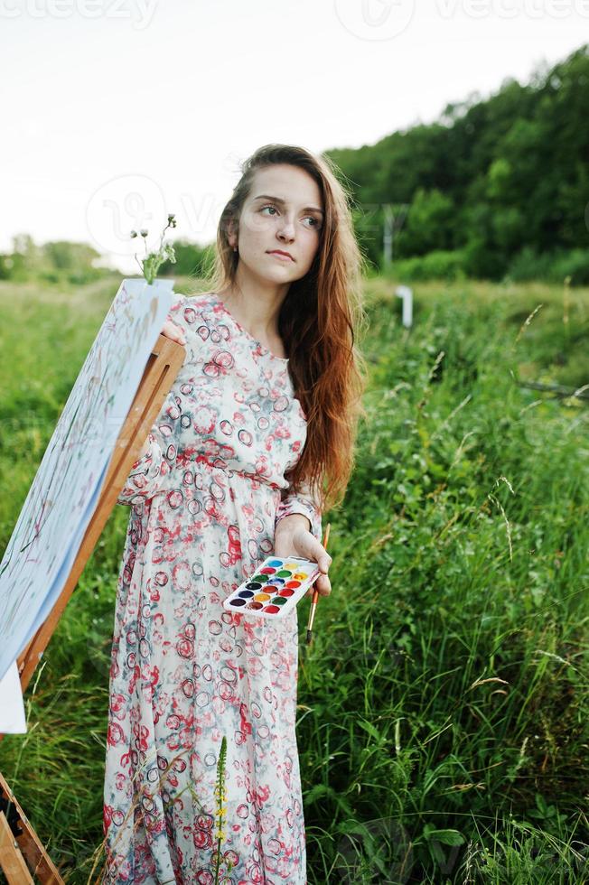 Portrait of an attractive young woman in long dress painting with watercolor in nature. photo