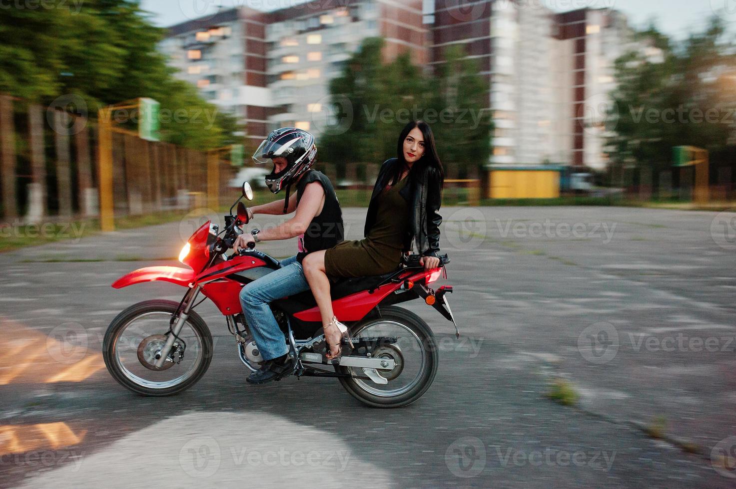 Woman in dress and leather jacket riding a motorbike with another man. photo