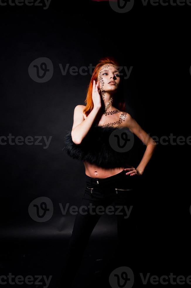 Fashion model red haired girl with originally make up like leopard predator isolated on black. Studio portrait. photo