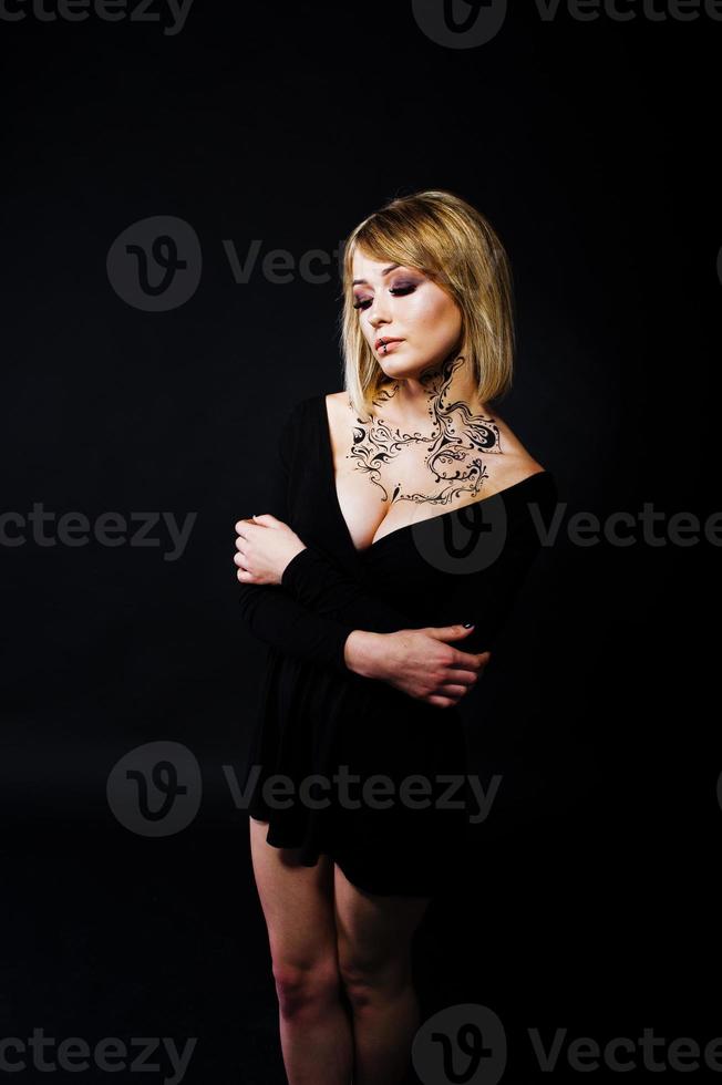 Studio portrait of blonde girl with originally make up on neck, wear on black dress at dark background. photo