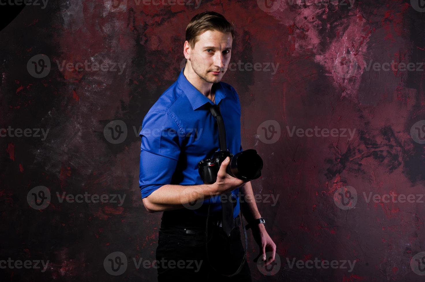 Studio portrait of stylish professional photographer man with camera, wear on blue shirt and necktie. photo