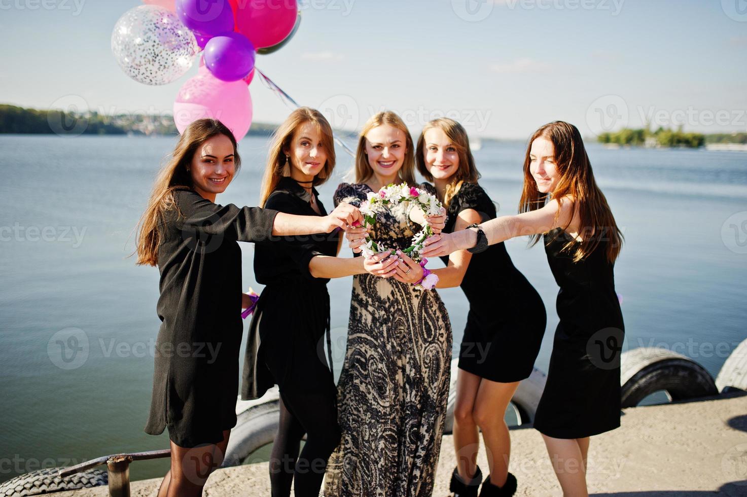 Five girls wear on black having fun against lake at hen party. photo