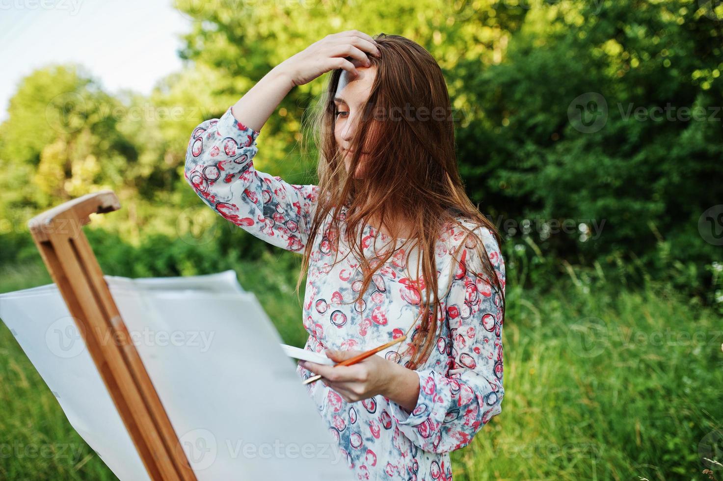 Portrait of an attractive young woman in long dress painting with watercolor in nature. photo