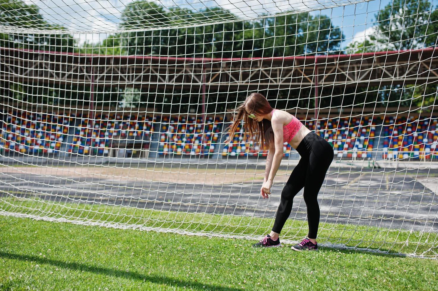 Fitness sporty girl in sportswear and sunglasses posed at stadium football gates outdoor sports. Happy sexy woman. photo