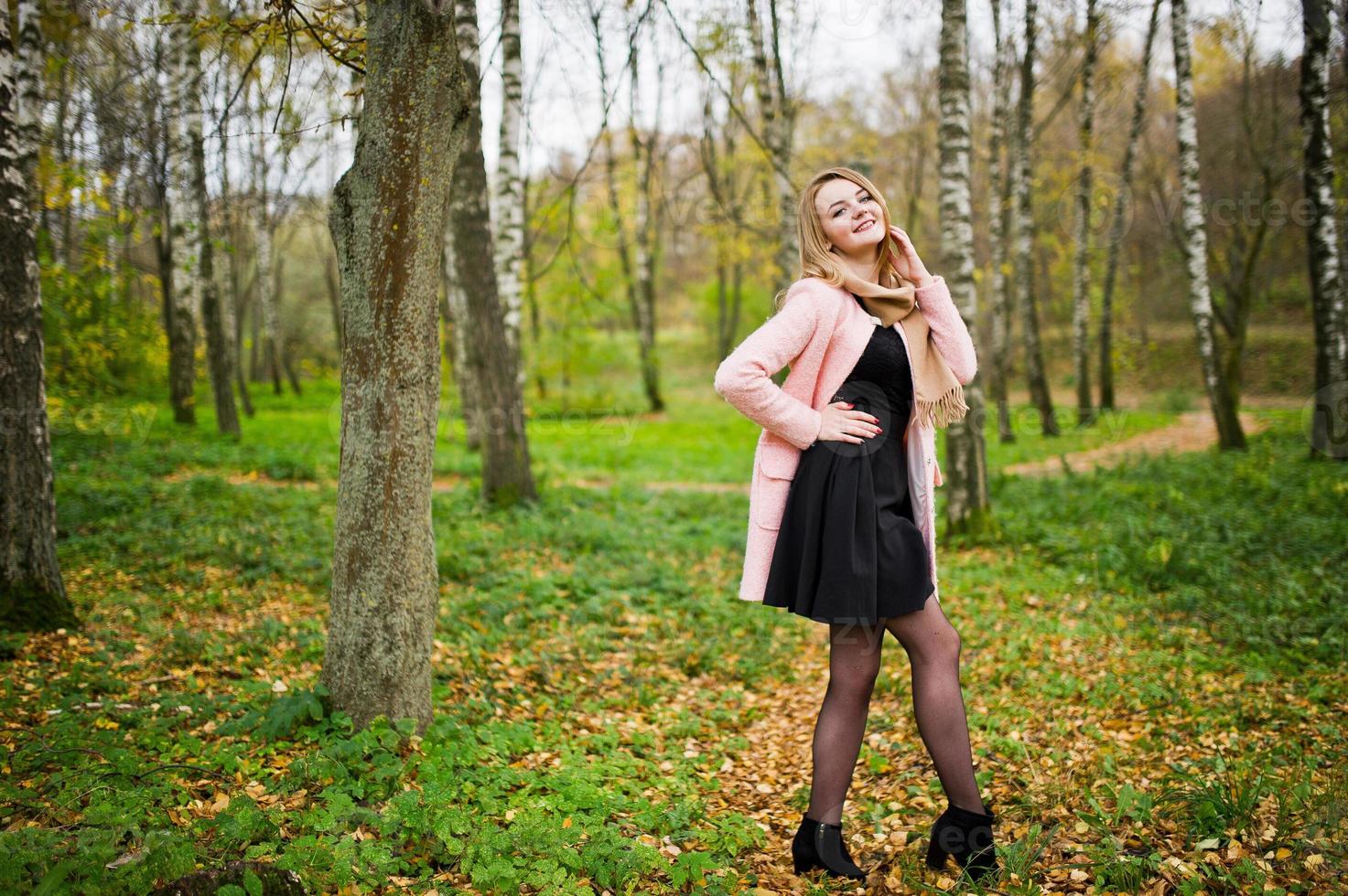 Young blonde girl at pink coat posed on autumn park. photo