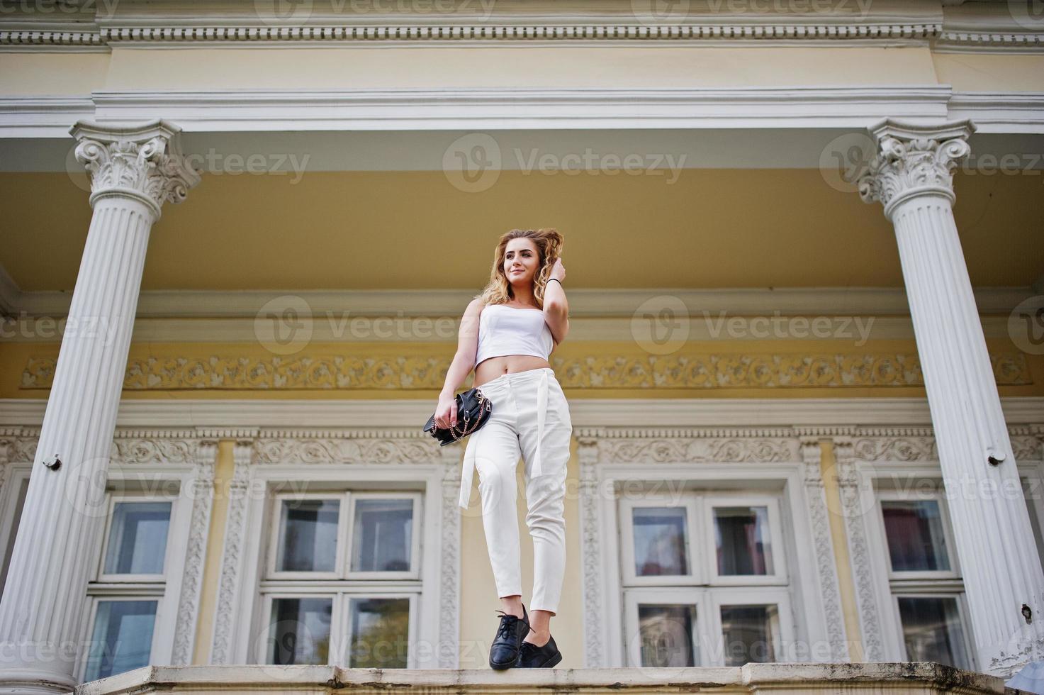 Stylish curly blonde model girl wear on white posing against old vintage house. photo