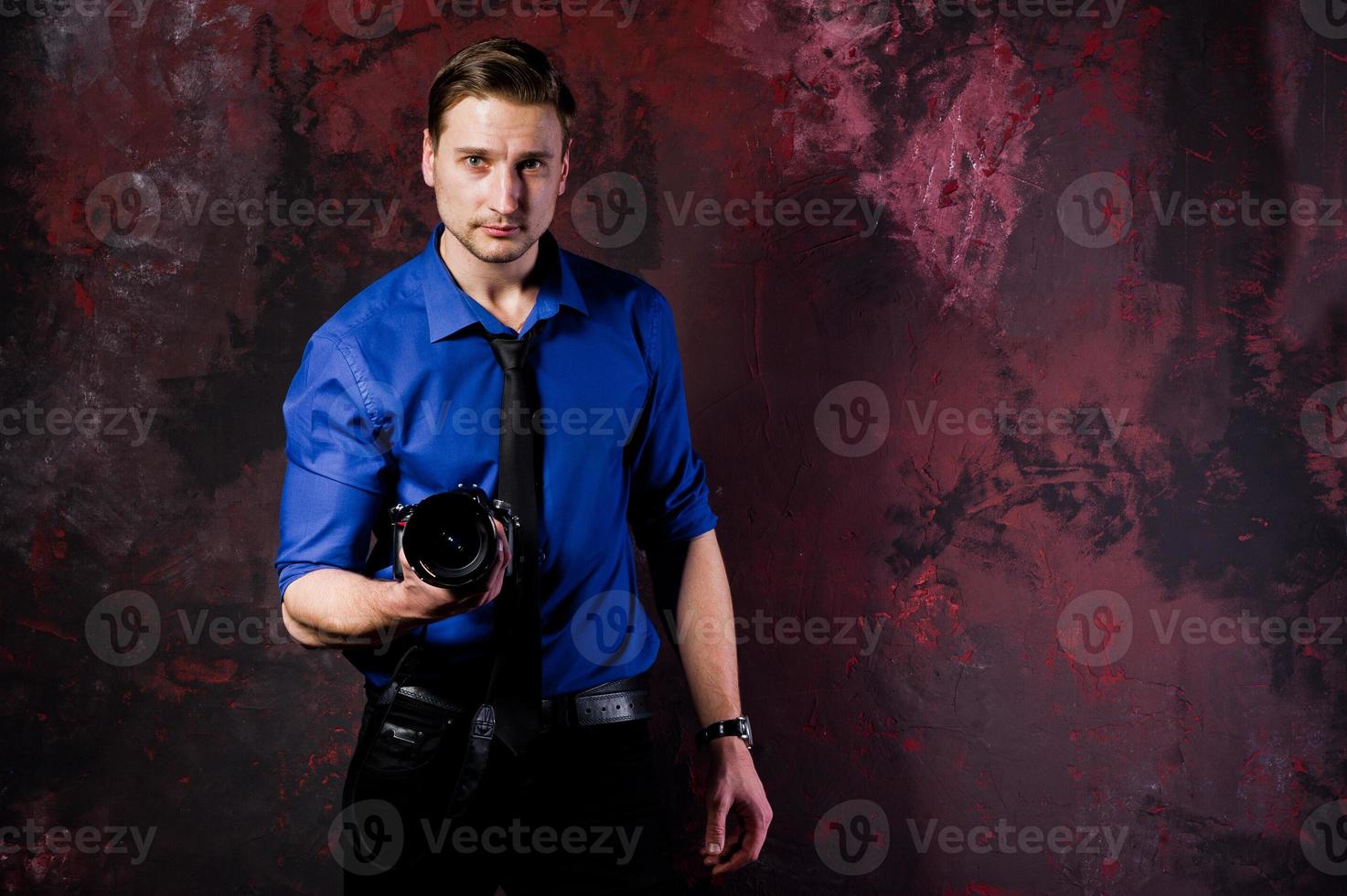 Studio portrait of stylish professional photographer man with camera, wear on blue shirt and necktie. photo