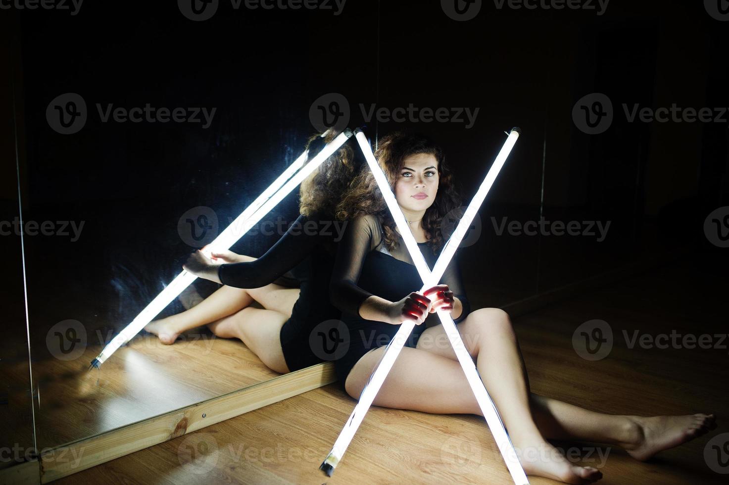 Curly brunette plus size model with two long led lamp at dance room with mirror. photo