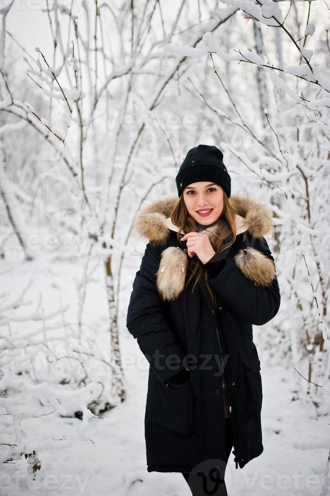 Beautiful brunette girl in winter warm clothing. Model on winter jacket and black hat. photo