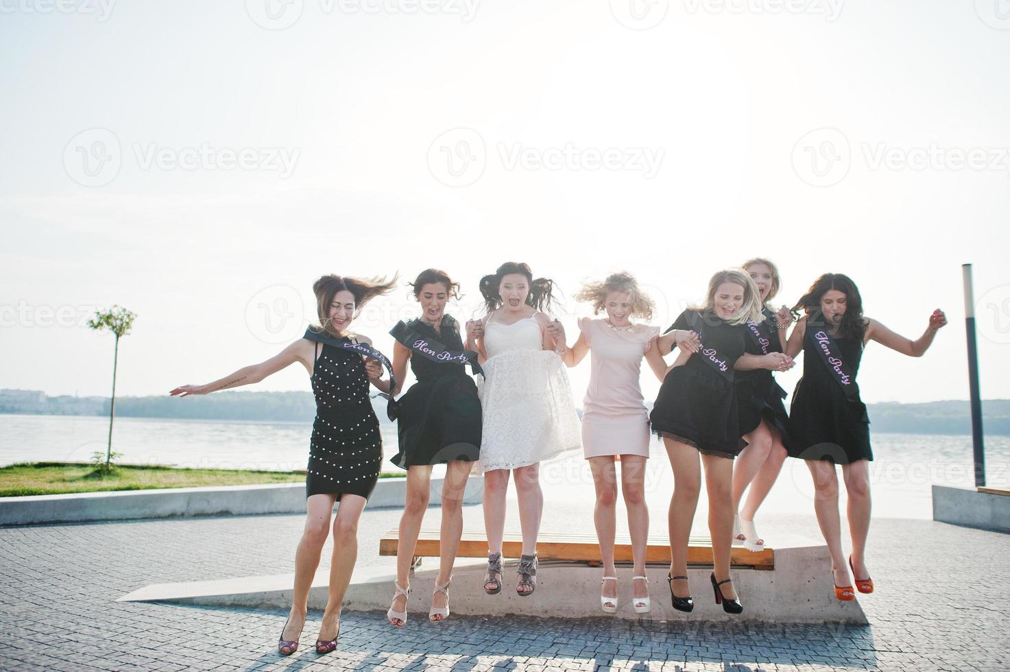 Group of 7 girls wear on black and 2 brides jumping at hen party. photo