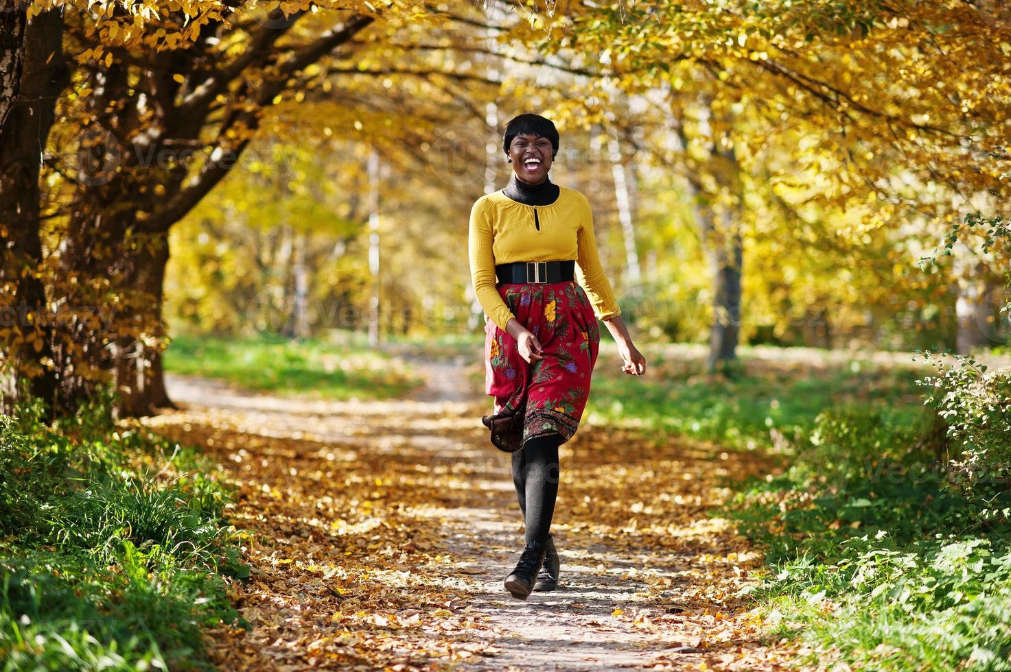 niña afroamericana con vestido amarillo y rojo en el parque de otoño dorado. foto