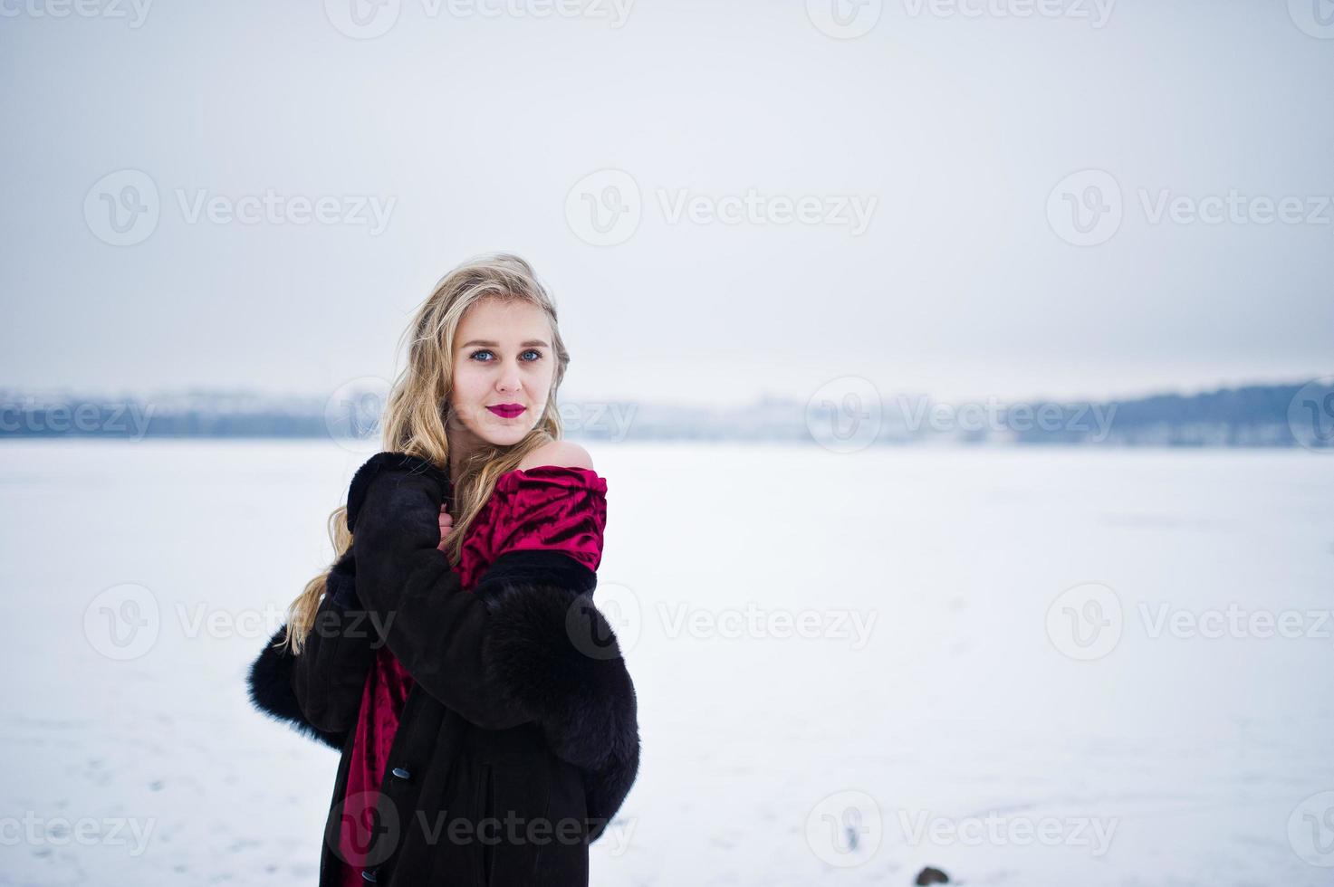 chica rubia de elegancia en abrigo de piel y vestido de noche rojo posó en el día de nieve de invierno. foto